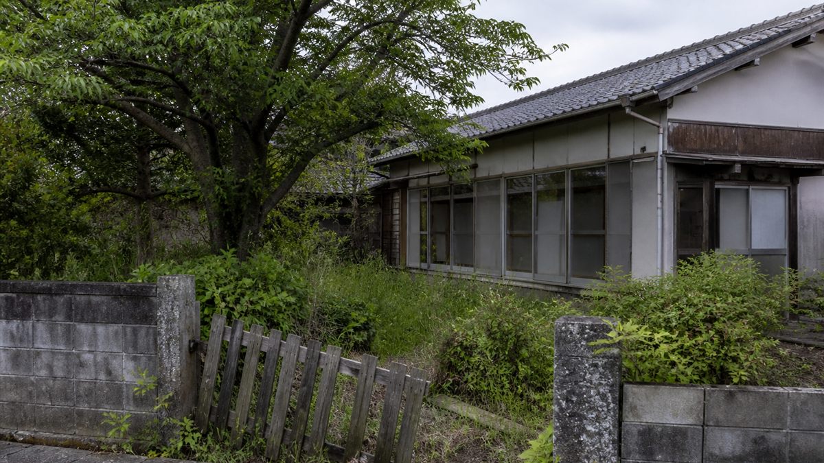 傾いた塀と伸びた庭木のある空き家