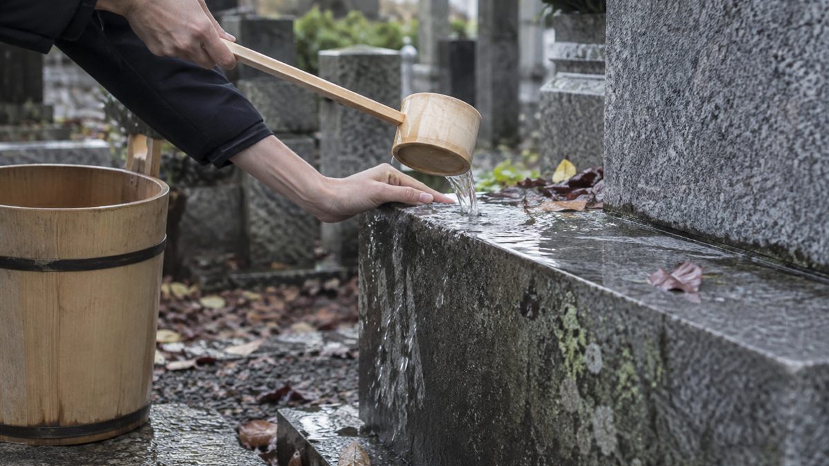 手桶と柄杓で墓石の脇を清めている手元