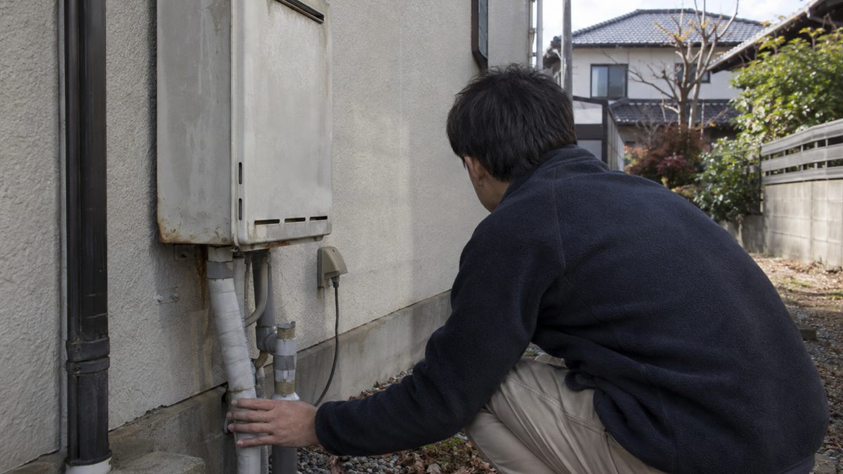 屋外の給湯器と電源の接続部分を目視で確かめている場面