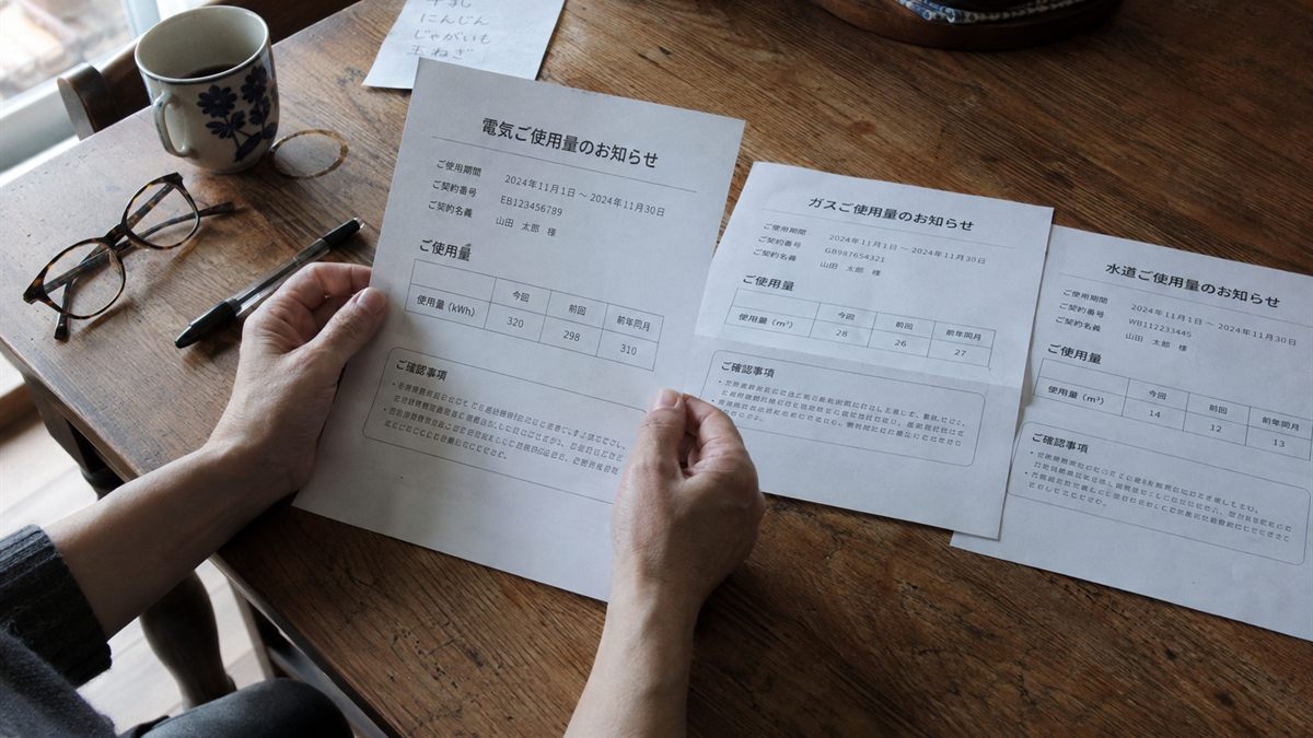 食卓に電気・ガス・水道の請求書を並べて確かめている手元