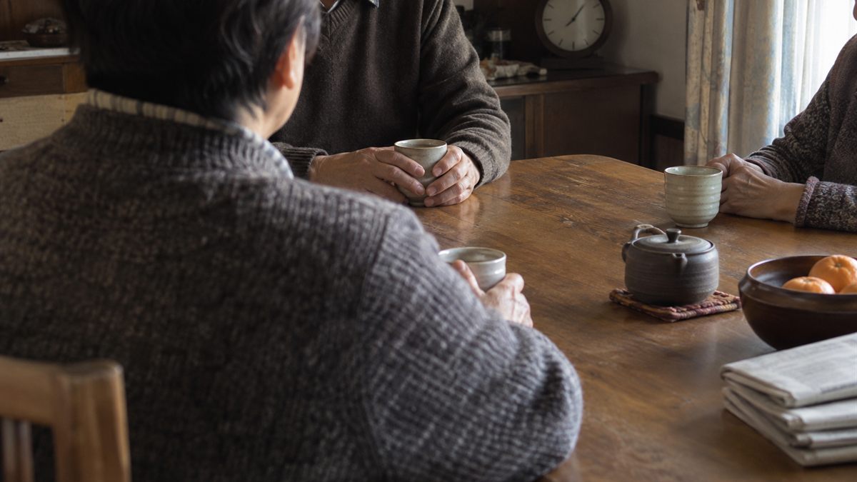 実家の食卓で家族が向かい合って話している場面