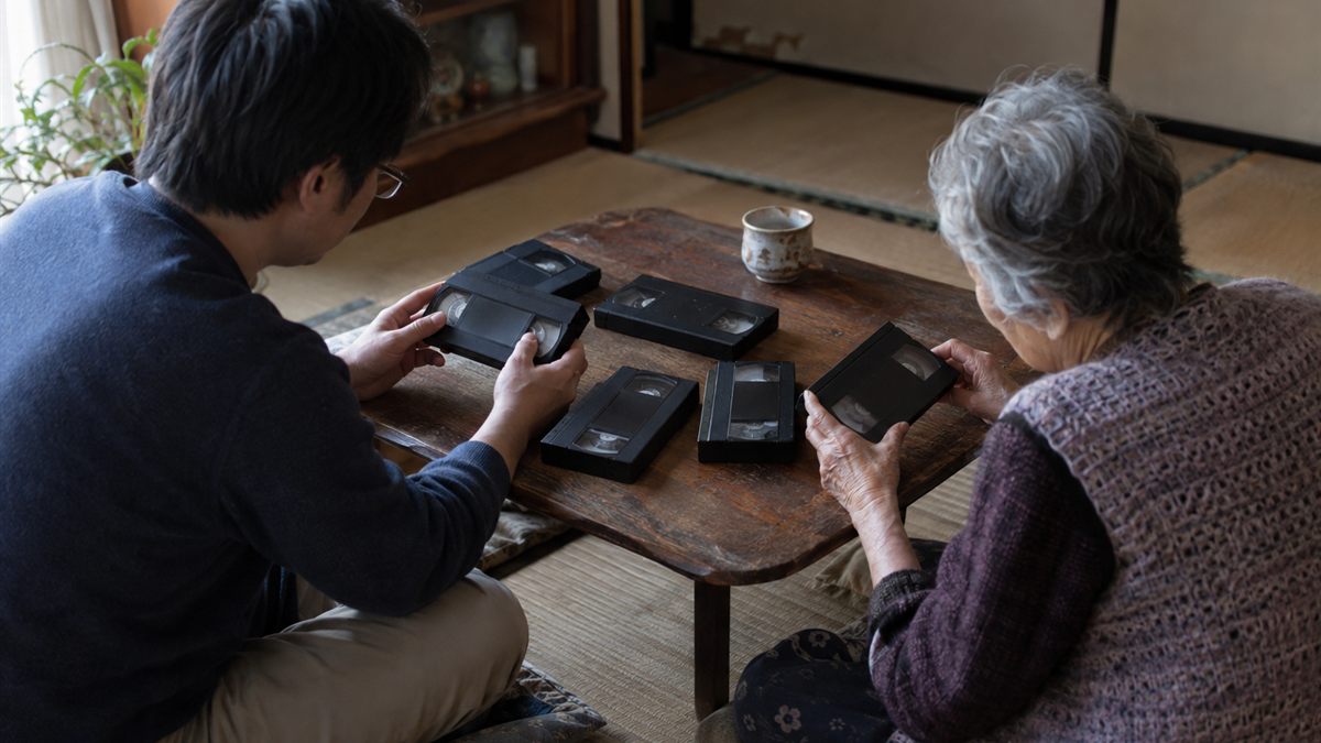 机に並べたビデオテープを親子で手に取って相談している場面