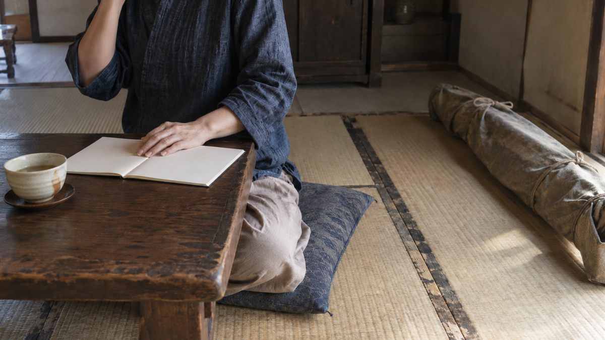 畳の部屋で、布に包まれた細長い包みを前に電話をかけている人